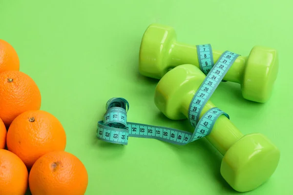 Naranjas cerca de pesas, cinta métrica cyan sobre fondo verde — Foto de Stock