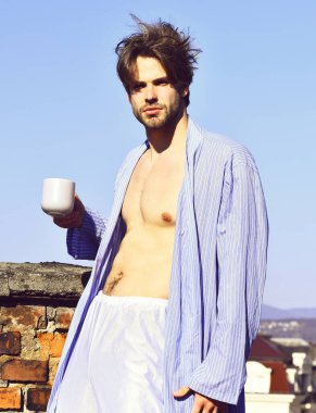 Mavi çizgili pijamalı, elinde fincanla beyaz maço.