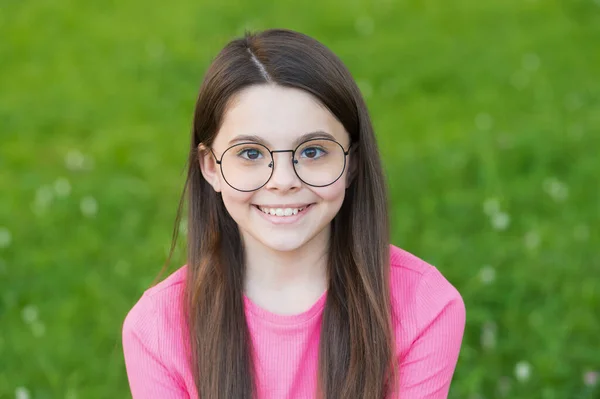 Piccola bellezza con un sorriso felice. Bambino seduto sull'erba verde. Il bambino si rilassa durante l'estate all'aperto. Look alla moda di piccola modella. Bellezza e moda. Vacanze estive. Vacanza e tempo libero — Foto Stock