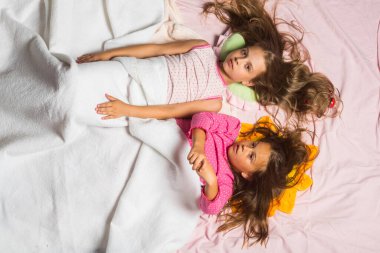 Pembe pijamalı çocuklar yastıkların üzerinde yatıyor.