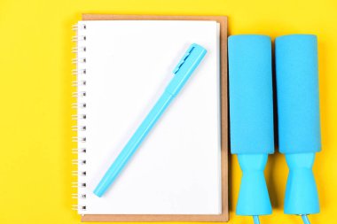 Not defteri, kalem ve spor aletleri sarı arka planda üst görünüm