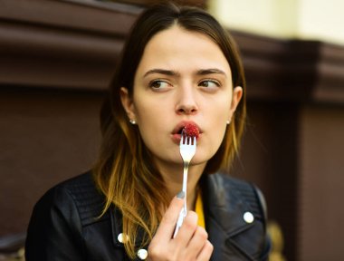 Tatlı çatalını ağzının yanında ahududuyla tutan kadın yan bakıyor..