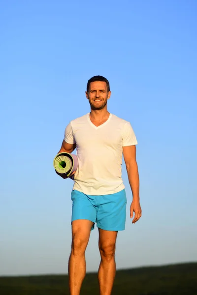 Man met sportieve figuur en lachend gelaat houdt fitnessdeken. — Stockfoto