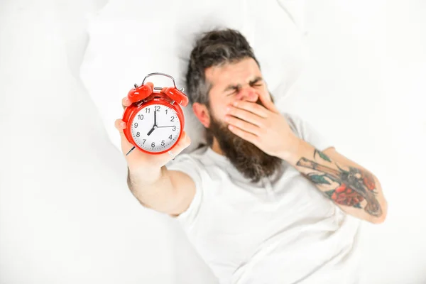 泣き顔の男は枕の上に横になり目覚まし時計を持っている. — ストック写真