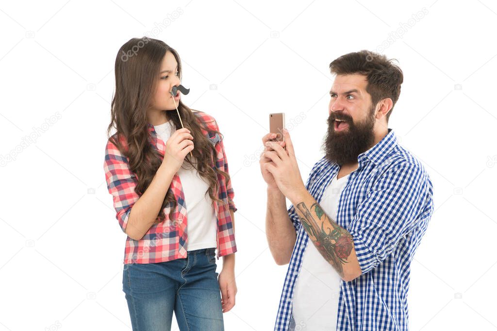 Take photo. Creative team. Bearded man take photo of small child. Girl posing with mustache props. Hipster use smartphone mobile camera. Family celebration. Family photo session. Family goals