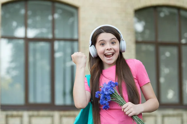 Es la manera correcta de celebrar. Un niño feliz hace un gesto ganador. La niña sostiene flores escuchando música. Celebración del aniversario. Celebración de cumpleaños. Celebración festiva. Llama a la celebración — Foto de Stock