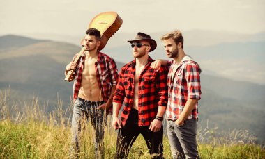 Macera Takımı. Uzun yol. Turistler yürüyüş konsepti. Arkadaşlarla yürüyüş. Güneşli bir günde gitar çalan adamlar. Kareli gömlekli bir grup genç dağın tepesinde birlikte yürüyorlar.