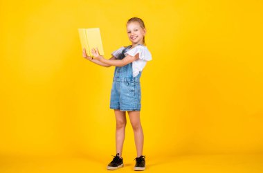 Çocuklar için edebiyat. Sarı arka planda gözbebeği. Zeki görünüşlü ve sıradan giyimli bir çocuk. Modern eğitim konsepti. Fikirden esinlendim Kız kitabı okudu. Okula ve çocukluk konseptine dönelim.