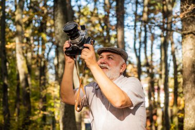 Profesyonel için en iyi kamera. Sonbahar gününde yaşlı fotoğrafçı. Emeklilerin elinde eski model kamera var. Fotoğraf makinesi olan yaşlı bir adam. Çekim için analog kamera kullanılıyor. Doğa fotoğraf çekimi oturumu