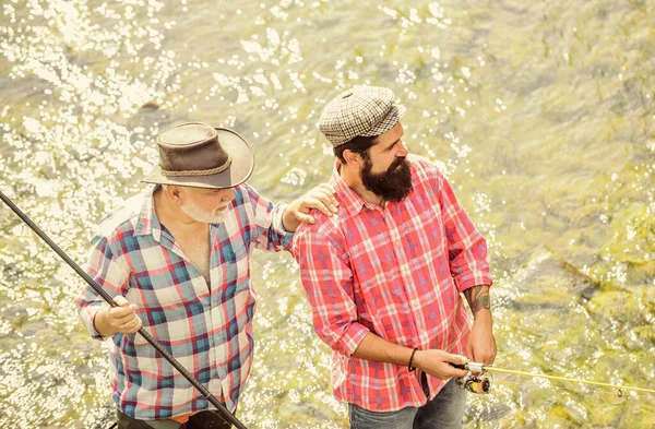 Karierte Mode. Fischer mit Angel und Netz. Zelten am Ufer des Sees. Vater und Sohn angeln. Wilderei. Konzept eines ländlichen Kurzurlaubs. Hobby. Wilde Natur. Großwildfischen. Freundschaft — Stockfoto