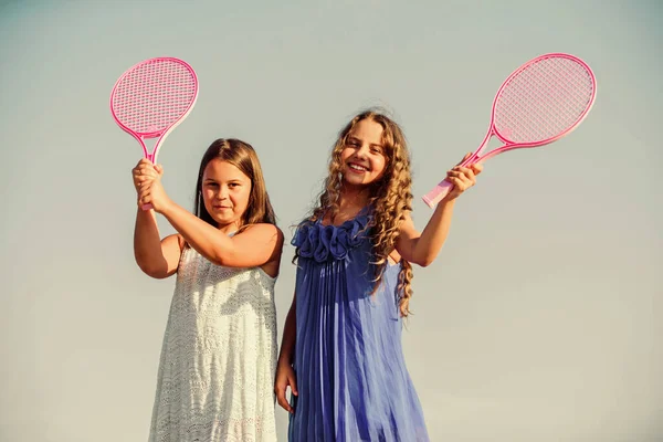 Vida activa. As crianças jogam tênis fundo céu azul. Miúdos desportivos. Meninas pequenas com raquete de tênis rosa. Lazer. Jogo desportivo. Miúdos divertidos e alegres. Feliz infância. Positivo. Equipa de meninas — Fotografia de Stock