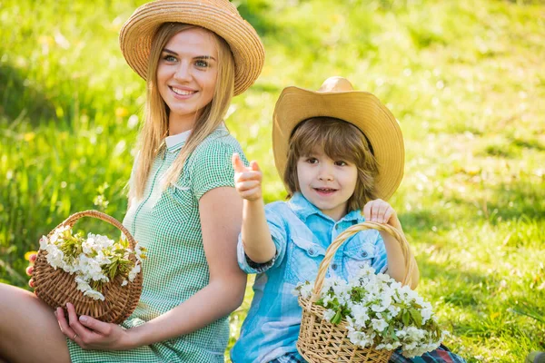 Concept de ranch. Fleurs sauvages dans les champs. Joyeuses fêtes. Mère et mignon fils portent des chapeaux de paille. Ferme familiale. Belle famille en plein air fond de nature. Famille Cowboy ramassant des fleurs dans des paniers — Photo