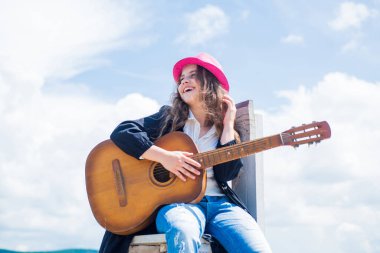 Yetenekli çocuk. Country müzik tarzı. müzik enstrümanı. Akustik gitarla çal. Küçük kız gitar çalıyor. Müziği seviyor. Müzik okulu dersleri. Gökyüzü arkaplanındaki küçük gitarist