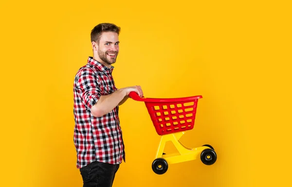 Funny man with small shopping cart. weekend on buying products. rejoices successful purchases. spends money unwisely. customer pushing cart. buyer in supermarket. empty toy trolley. man go shopping — Stock Photo, Image