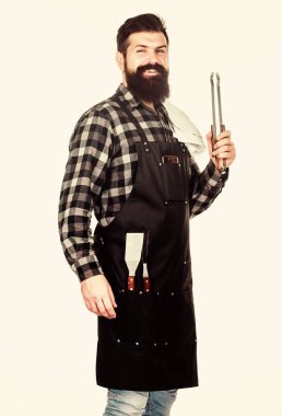 Adam mutfak aletlerini barbeküde tutuyor. Açık havada et kızartmak için aletler. Piknik ve barbekü. Parkta et pişiriyorum. Barbekü ustası. Sakallı hippi barbekü için önlük giyer. Kızartma ve ızgara yemek.