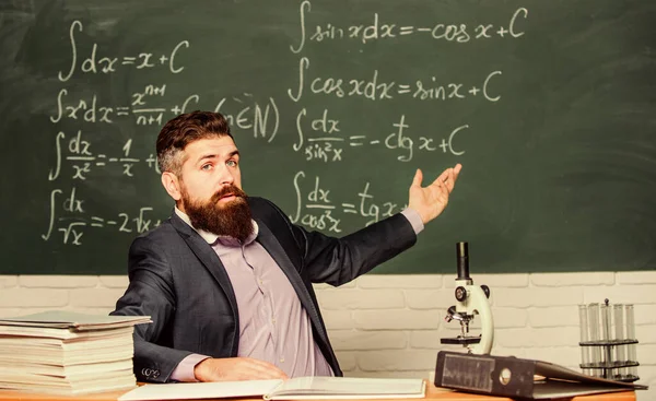 Talking to students or pupils. School teacher concept. Teacher bearded man tell interesting story. Teacher charismatic hipster sit at table classroom chalkboard background. Educational conversation
