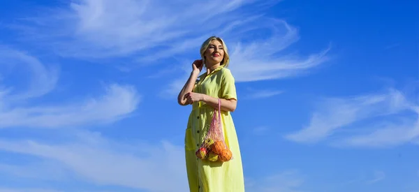 Milieubewust. Vrouw draagt groenten en fruit in eco tas. Geen verspilling. Kunststof vrij concept. Duurzame levensstijl. Herbruikbare katoenen en mesh eco tassen om te winkelen. meisje zomer dag blauw hemel achtergrond — Stockfoto