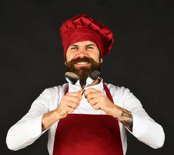 Homem com barba segura utensílios de cozinha em fundo preto . — Fotografia de Stock