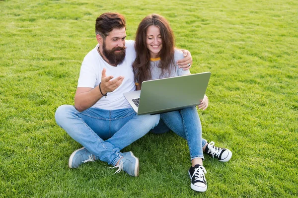 Modern entertainment. Bearded man and sexy woman use laptop. Couple in love rest on green grass. Enjoying modern computer technology. Modern life. Social media. Modern leisure. Summer vacation