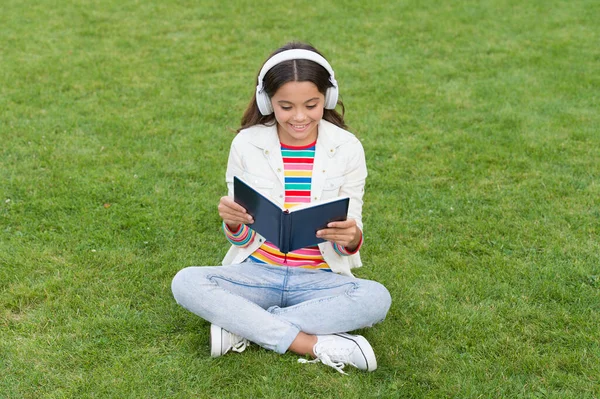 Sois un bon acharné. journée de la connaissance. future éducation scolaire. adolescent fille avec livre sur l'herbe verte. jolie enfant petite fille lire le livre. étudier la littérature pour les enfants. les nouvelles technologies dans la vie numérique — Photo