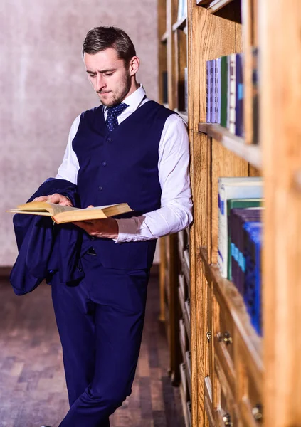 Étudiant lit livre près des étagères, déconcentré. Étudiant ou homme intelligent — Photo