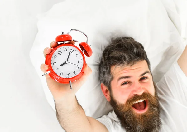 El hombre con la cara feliz yace en la almohada, sostiene el despertador . —  Fotos de Stock