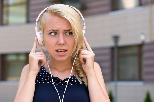 Mujer con cara confusa escuchando música. Mujer con cabello rubio — Foto de Stock
