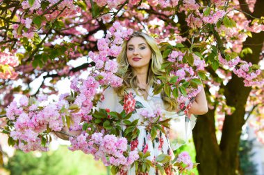 Mükemmel bir bahar günü. Doğal güzellik ve kozmetik. Kadın çiçek parfümü. Bahar doğasının güzelliği. Makyajlı çekici kadın. Kızın uzun kıvırcık sarı saçları var. Sağlıklı güzellik. pembe sakura çiçekleri