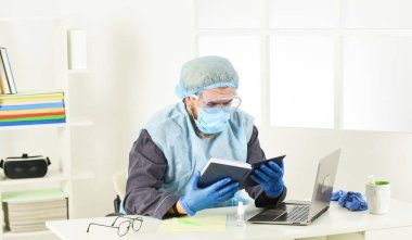Kitabı oku. Adam solunum maskesi, eldiven ve koruyucu gözlük takıyor. Evde güvende kal. Koronavirüs salgını. Hijyen kilitlendi. uzaktan çalışma konsepti. Sıhhi doktor üniformalı bir adam.
