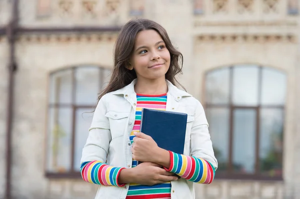 Libro de la biblioteca. Visitar la biblioteca puede fomentar la lectura y la exploración en los niños. Interesante historia para el niño. Concepto de tarea. La niña sostiene el libro. Niña con libro de fondo urbano — Foto de Stock