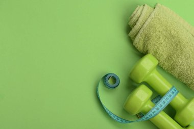 Yeşil renkli dambıllar, bükülmüş mezura ve havlu.