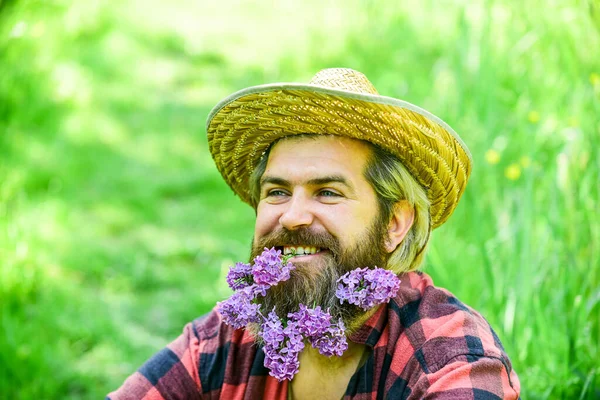 Umweltfreundliches Lifestylekonzept. Rustikale Mann mit Bart glückliches Gesicht genießen das Leben in ökologischer Umgebung. Hipster mit lila Blüten sehen glücklich aus. Bärtiger Mann mit fliederfarbenem Bart im grünen Grashintergrund — Stockfoto