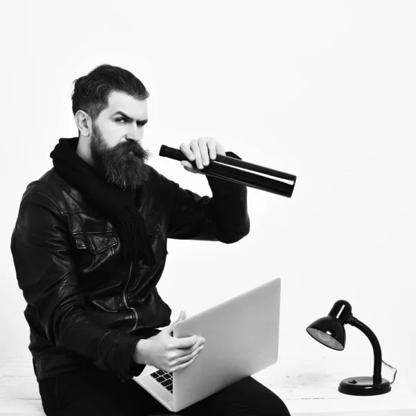 Skäggig brutal kaukasisk hipster sitter på bordet med bärbar dator — Stockfoto