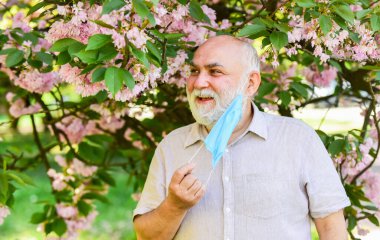Astım tedavisi konsepti. Polen alerjeni. İnsan ve çiçekler. Solunum durumu. Nefes almakta zorlanıyorum. Alerjik reaksiyon. Enfeksiyonun yayılma riskini sınırla. Kıdemli adam maskesi. Solunum maskesi