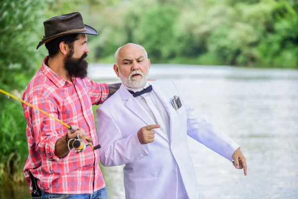 Instructor personal. Hombre barbudo y elegante hombre de negocios pescan juntos. Habilidades de pesca. Hombres amigos relajante fondo de la naturaleza. Aprende a pescar. Pescado con acompañante que puede ofrecer ayuda en caso de emergencia —  Fotos de Stock