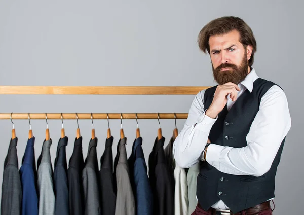 Man clothing in boutique. Man with suit. tailor in his workshop. Handsome bearded fashion man in classical costume suit. Man in custom tailored suit presenting expensive tuxedo. Another client