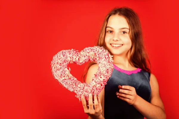 Creas mi sonrisa de corazón. Niño feliz con el corazón rojo de fondo. Niña con corazón de mimbre rosa. Decoración en forma de corazón para el día de San Valentín. Vacaciones de amor y cuidado, espacio de copia — Foto de Stock