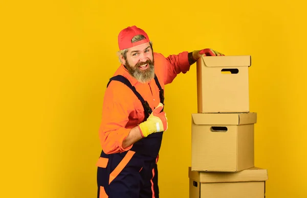 Umzug in eine neue Wohnung. Post. Bartträger in Uniform. Immobilien. Bewegender Tag. Sanierungsvorbereitungen. Drinnen bärtige Hipster. Umzugskartons auspacken. Bärtiger Mann Kurier hält Kisten — Stockfoto