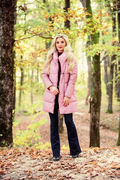 Puffer divat koncepció. Divatos szőke lány sétál az őszi erdőben. A nő meleg rózsaszín kabátot visel. Mindenkinek kellene kabát. A legjobb köpönyegforgató kabát. Hogyan rázzuk a golyóálló mellényt, mint egy csillag? — Stock Fotó