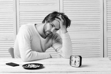 Adam ahşap masada çalar saat ve haplarla oturuyor.