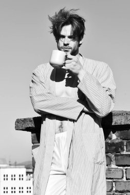 Mavi çizgili pijamalı, elinde fincanla beyaz maço.