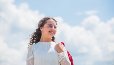 Küçük kız sırt çantası taşıyor. Güneşli arka planda küçük bir çocuk. Yaz ve bahar sezonu. Tatil ve tatil. Mutlu çocukluk. Okul çantasıyla gülümseyen öğrenci. Okula dönüyorum. Boşluğu kopyala