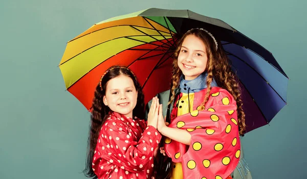 Счастливого детства. Яркий зонтик. Легче быть счастливыми вместе. Быть радугой в чьих-то облаках. Иди под зонтиком. Дети девочки счастливые друзья под зонтиком. Дождливая погода в подходящих одеждах — стоковое фото