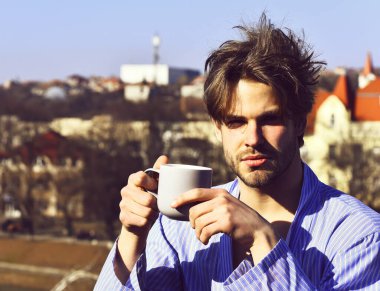 Mavi çizgili pijamalı, elinde fincanla beyaz maço.