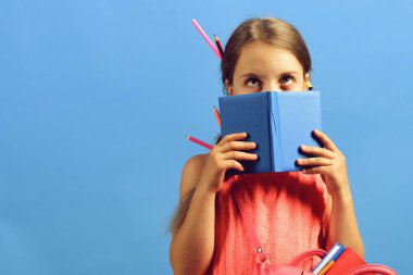 Kız mavi kitabın arkasına saklanıyor. Pembe elbiseli kız öğrenci.