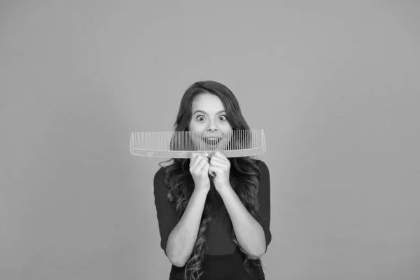 Cheerful smiling little kid with giant comb. Styling tips. Hairbrush for tangled hair. Having fun. Perfect hair. Large comb. Girl gorgeous long hair hold big comb. Hairdresser salon. Combing hair