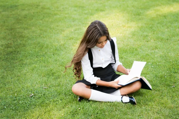Маленька дівчинка читає книжку. література для дітей. писати дитячі спогади. її щоденник. роблячи нотатки в блокноті. повернутися до школи. дитина навчається в парку. відпочити на зеленій траві з цікавою книгою — стокове фото