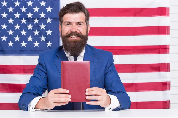 Olovo s jazykem. Student angličtiny. Šťastný hipster držet knihu na pozadí americké vlajky. Jazyková stipendia a granty. Jazykové vzdělávání dospělých. Vysokoškolské a vysokoškolské programy — Stock fotografie