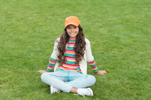 Posando para foto. bela estudante adolescente menina no parque. bonito sorrindo estudante confiante relaxar na grama verde. infância feliz. de volta à escola. Menina pequena usar roupas casuais. beleza e moda — Fotografia de Stock