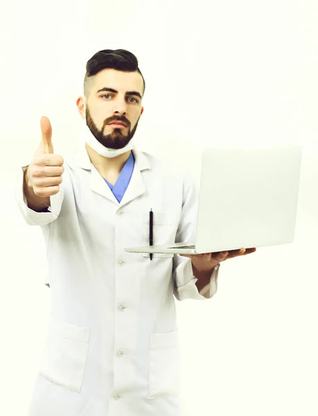 Orvos szakállal tartja fehér laptop és mutatja hüvelykujját fel — Stock Fotó